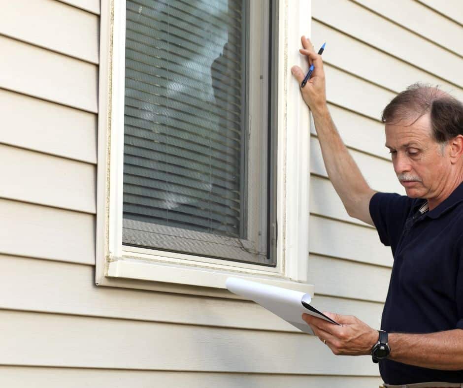 Man checking the window of a house and checking his checklist.