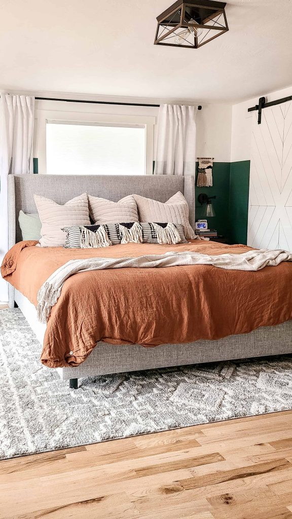 A view of our bohemian style dressed bed, with a neutral color pallet -- a rust colored duvet, cream throw blanket, and accent pillows at the head of the bed.