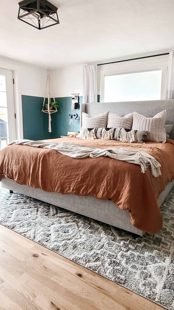 Another angle view of our king-size master bedroom bed, which is dressed in boho style bedding from Target. The duvet cover is a rich rust brown, and the rest of the bedding -- blankets and pillows -- are in a neutral cream and beige color palette. 