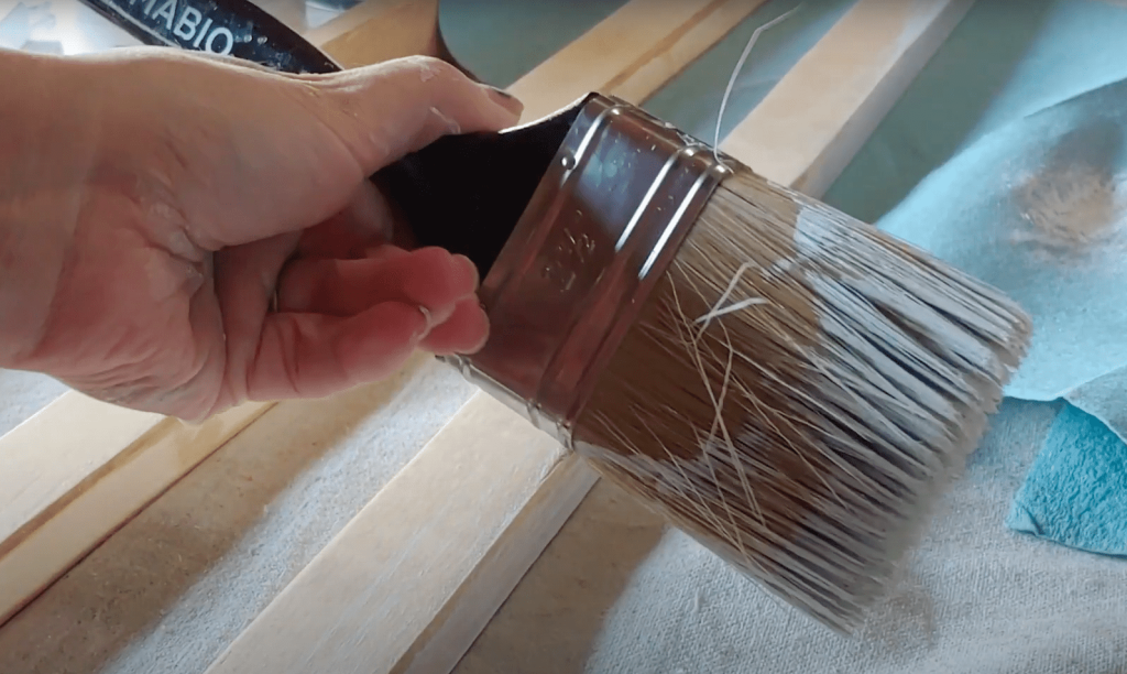 Woman holding a paint brush with white paint that has been blotted to create a dry brush painting effect.