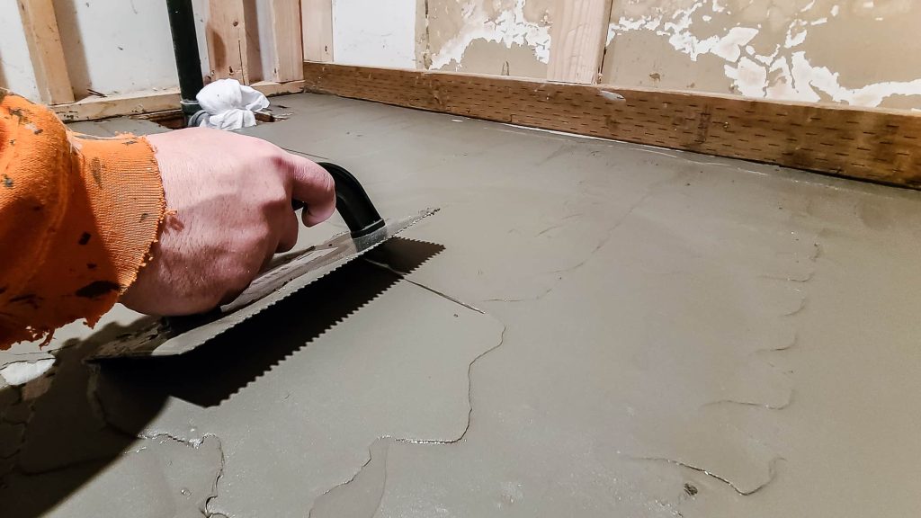 Spreading floor patch with a trowel for an even surface is key to how to install a bathtub.