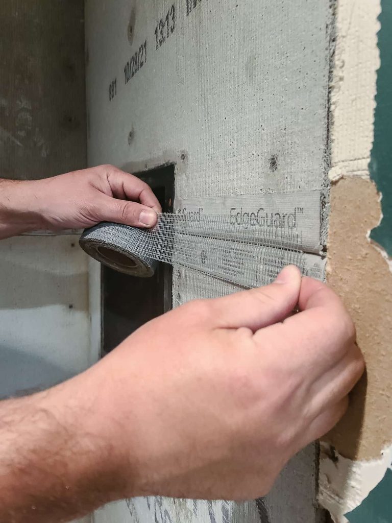 Adding mesh tape to cement board seam on the wall in the shower.
