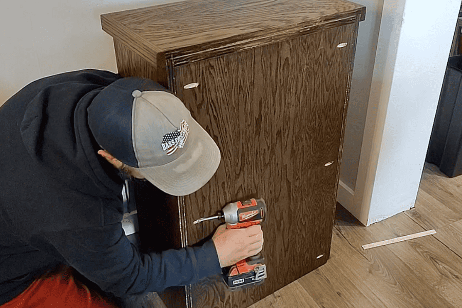 A man screws in the back panel of the trash cabinet for stability.
