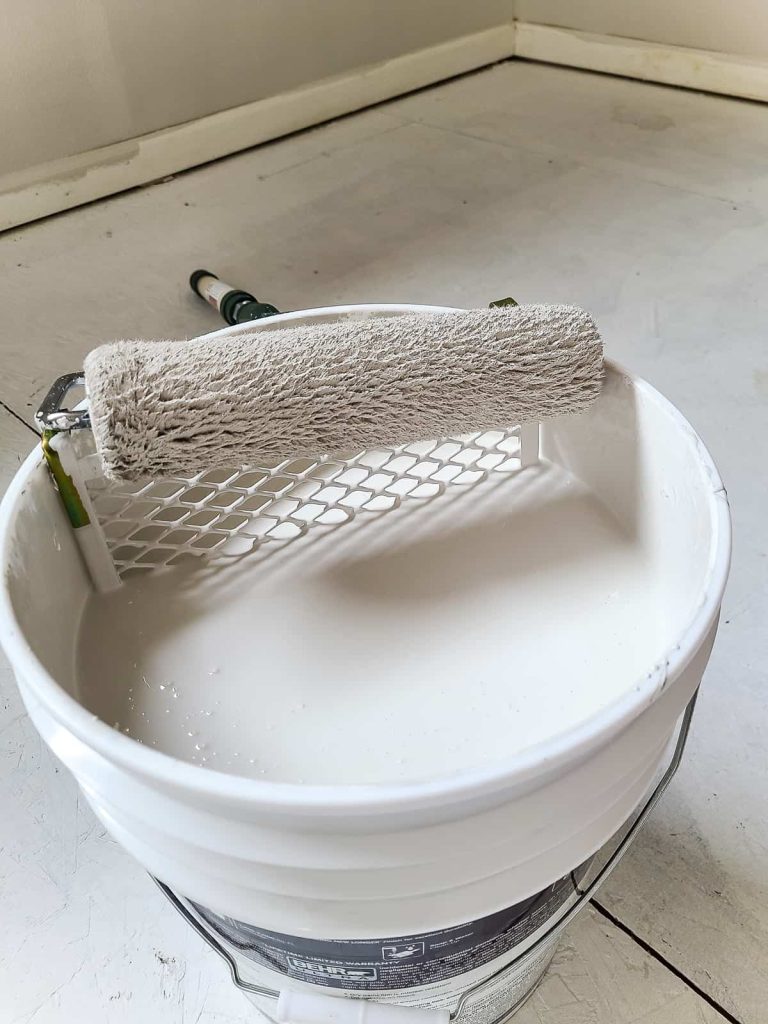 A photo of bucket of Behr Mineral white paint and a roller brush.