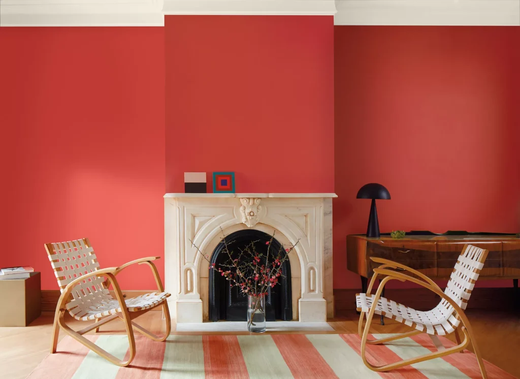 Benjamin Moore's color of the year for 2023 is Raspberry Blush, which is  the bright coral color painted on the walls in this sparse living room with marble fireplace and chairs 