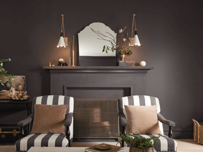 Darkroom is HGTV Home by Sherwin-Williams color of the year for 2023. it is a modern and moody dark paint color that has vintage vibes. it looks great when painted on the walls of this living room with a fireplace and accent chairs.