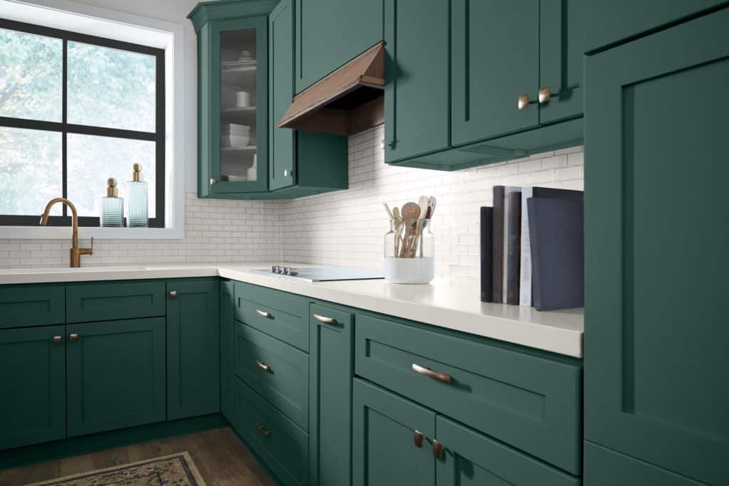 If you're looking for a bold green paint color to use on kitchen cabinets, try Dark Everglade from Behr Paint. It looks great here paired with brass hardware, cream backsplash and countertop. 