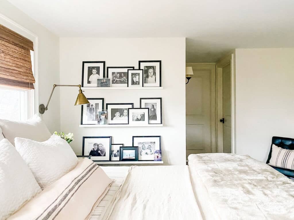 Behr Swiss coffee looks amazing painted on the walls of this bedroom from Most Lovely Things with white floating shelves filled with black and white pictures paired with white bedding on the bed