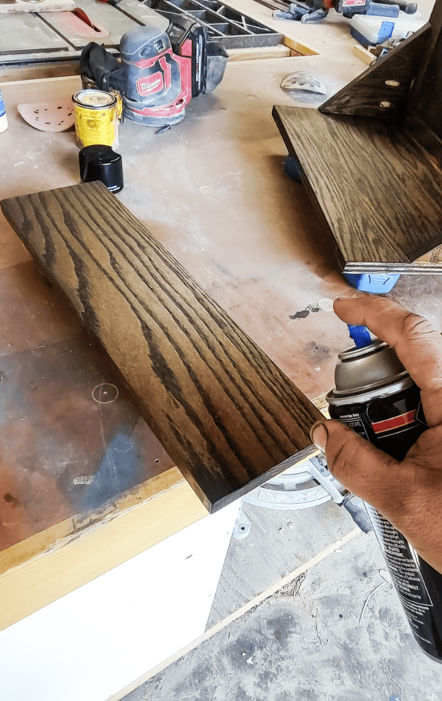 A man applies spray lacquer over the finished dry stain for a final touch.
