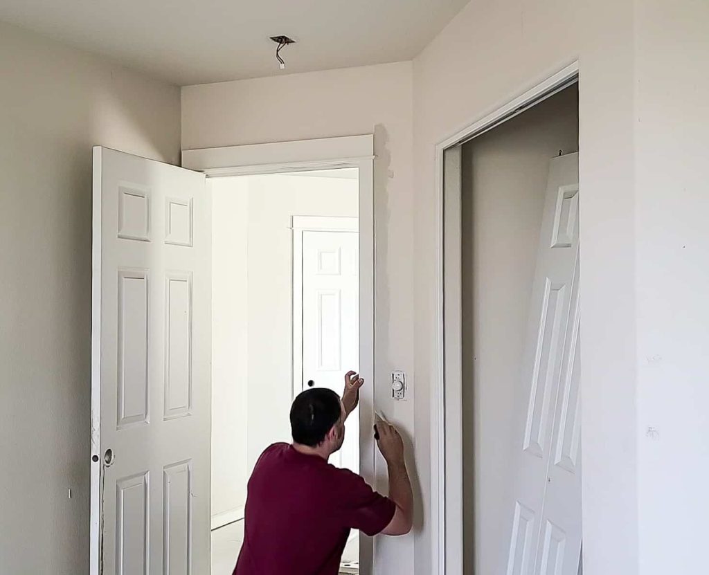 Man cutting in paint around the door to the bedroom 