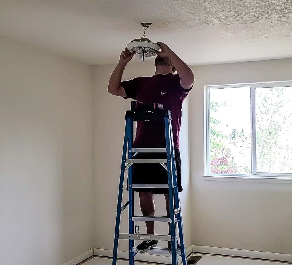 Man on a ladder removing overhead light fixture to be able to paint the ceiling