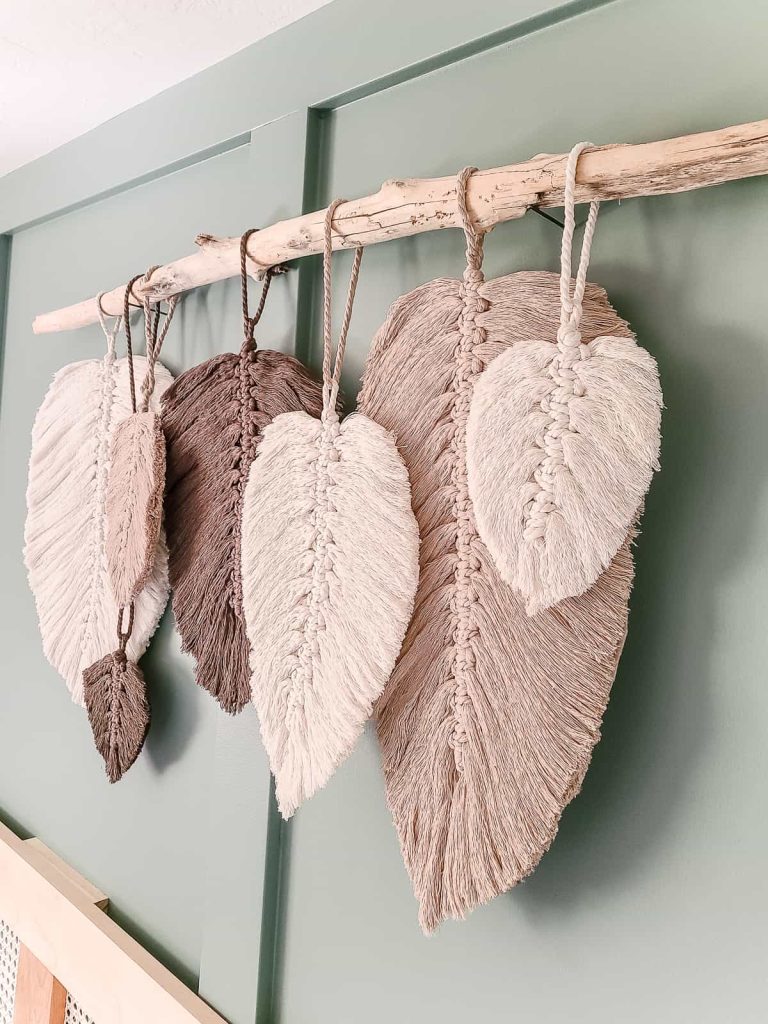 Macrame feather wall hanging above bed with seven feather in different sizes and shades of pink and white