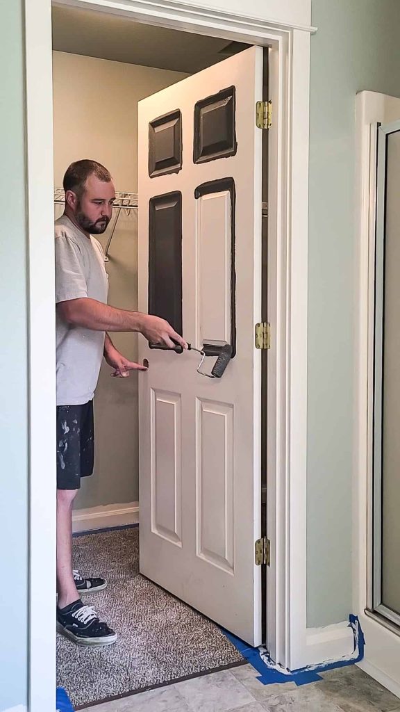 Man painting the closet door in the bedroom with a paint roller.