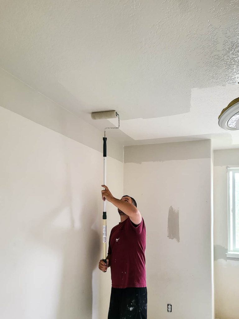 Man painting the ceiling with a paint roller on an extended paint pole.