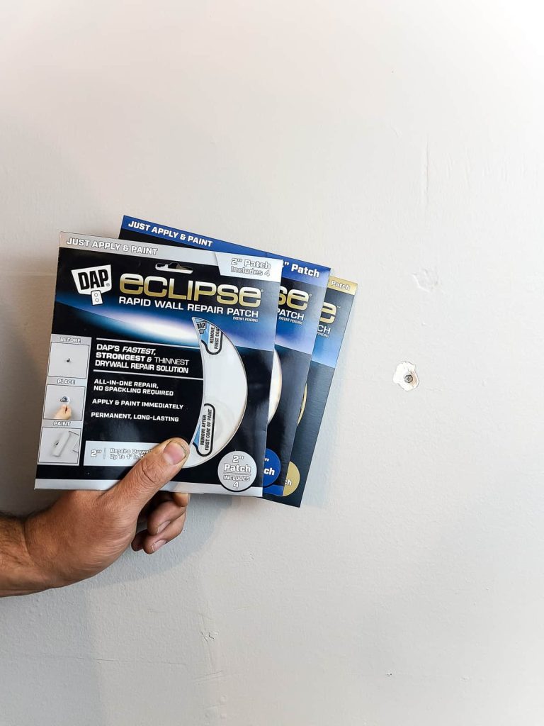 A person holds three DAP Eclipse rapid wall repair patch kits next to a small hole in a drywall wall.