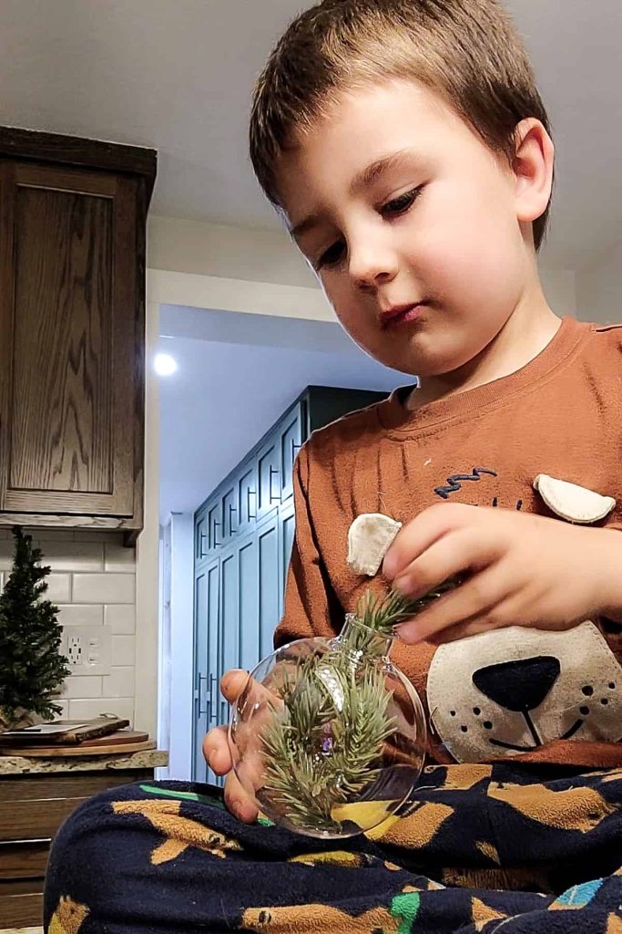 kid stuffing faux greenery inside clear plastic ornament