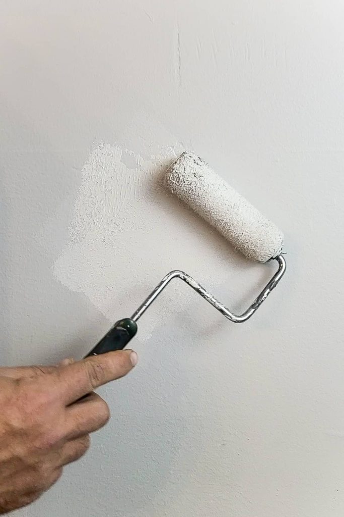 A person uses a small paint rolled to paint a fresh layer of paint, covering the transparent wall hole patch.