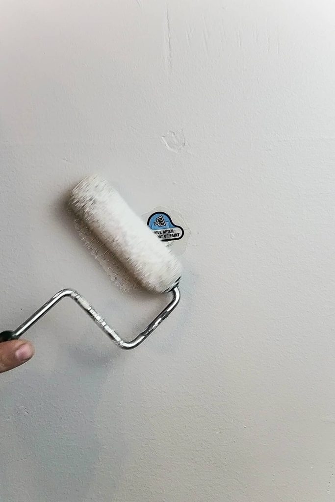 A person uses a small paint roller to apply a coat of paint over the wall hole patching sticker.