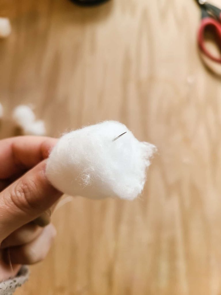 Needle pushing through cotton ball to make garland