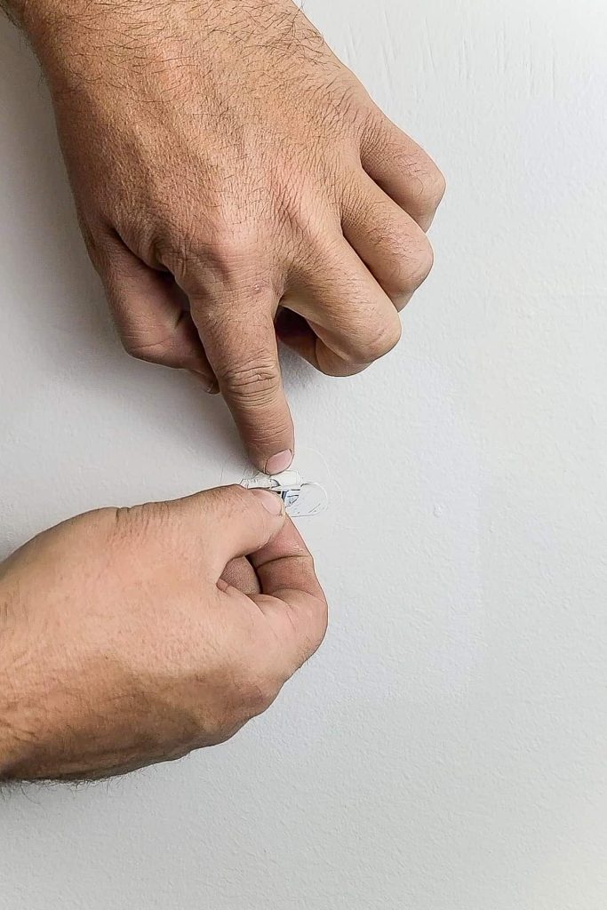 A person peels the protective DAP repair patch from the painted wall, revealing the semi-patched hole underneath.