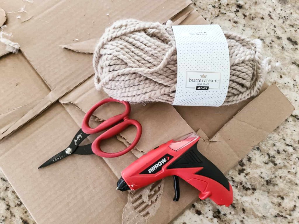 Supplies needed to make DIY stocking tags with cardboard scraps, scissors, hot glue gun and tan yarn