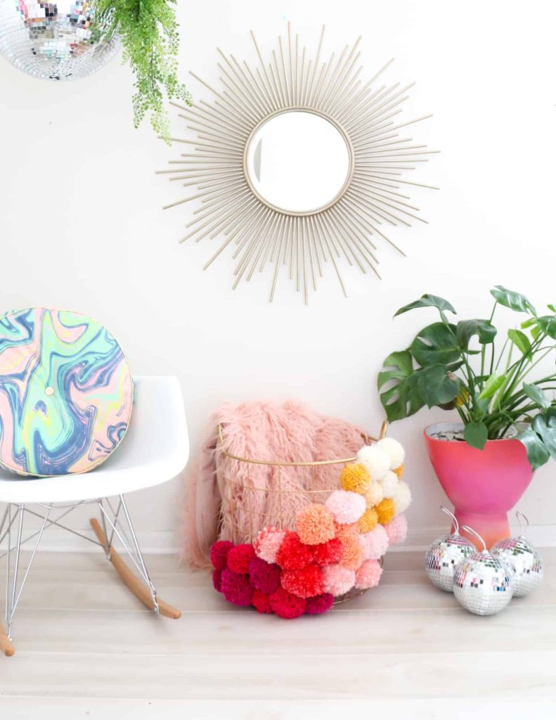 wire basket decorated with colorful yarn pom poms used for blanket storage