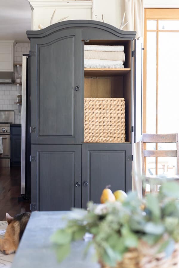 black armoire with blankets stored on the top shelf