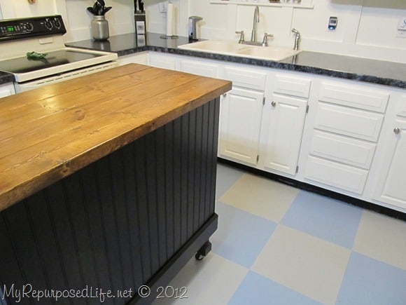 repurposed desk turned kitchen island painted dark with butcher block countertop surrounded by white cabinets 