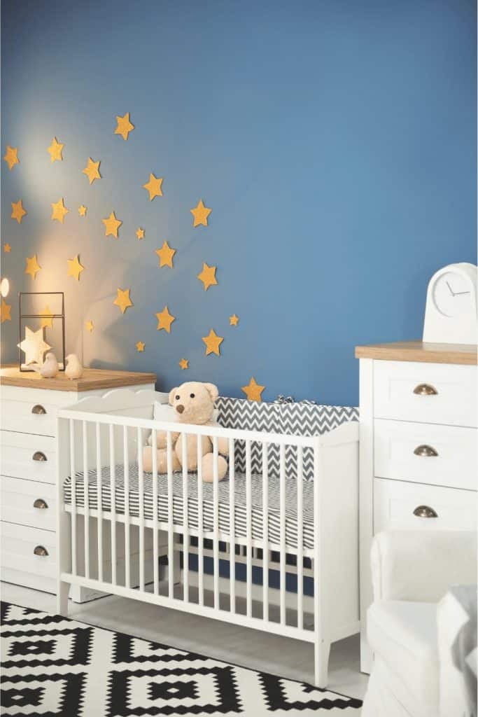 A Teddy bear in a crib in a nursery using blue on the walls for a boys room with stars as decoration.