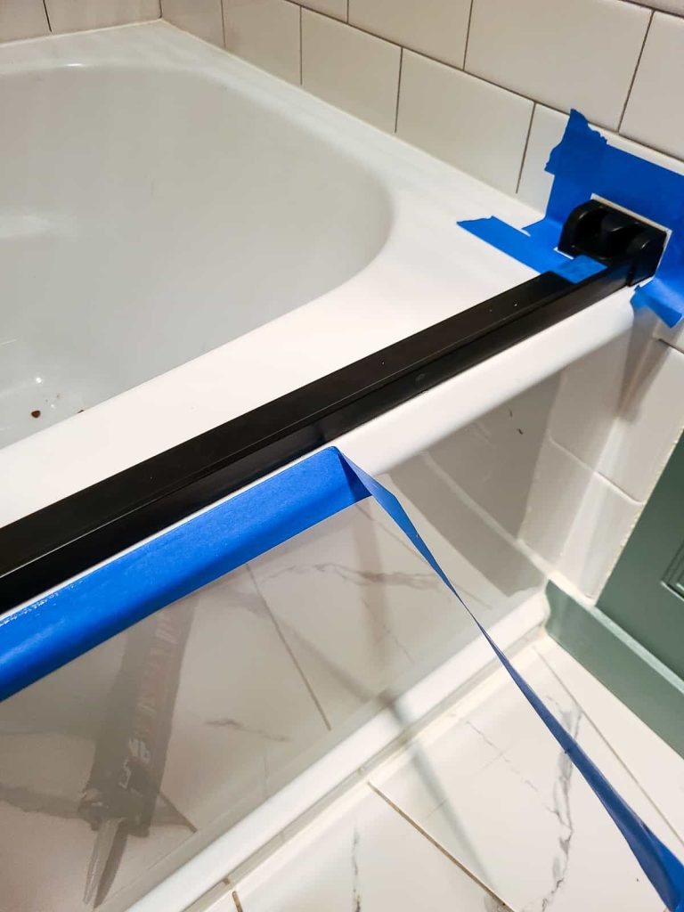 Removing tape to reveal a tooled water proof caulk seal as a part of a how to install a shower door tutorial