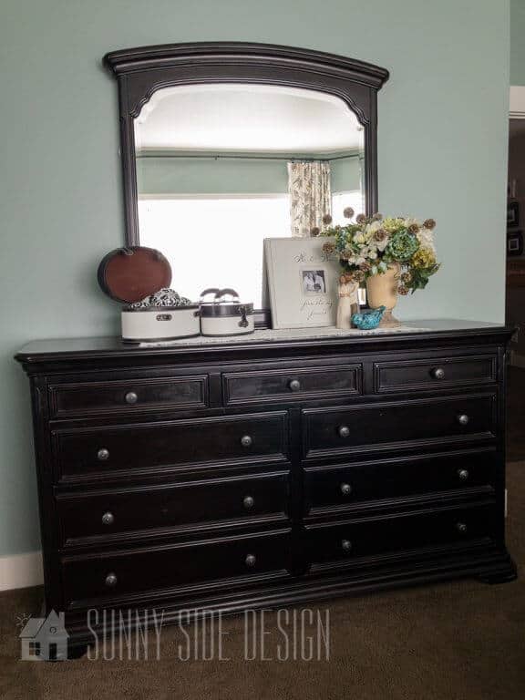 bedroom painted in light green behind a black dresser with mirror 