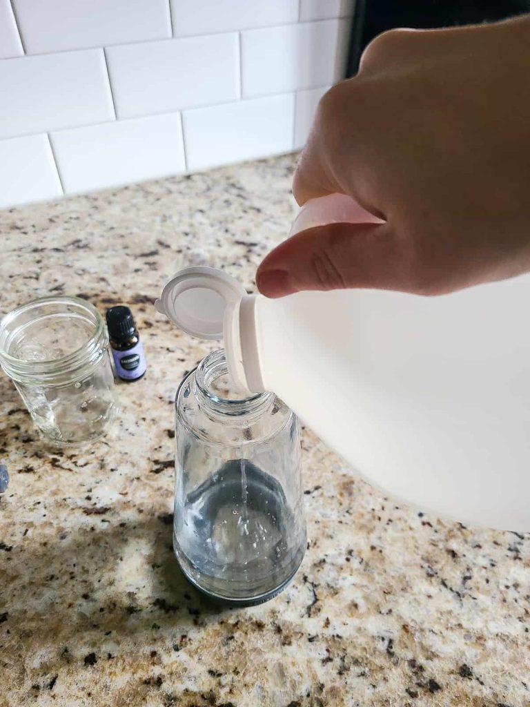 Adding vinegar to a glass bottle to start making a homemade cleaner for cleaning cabinets