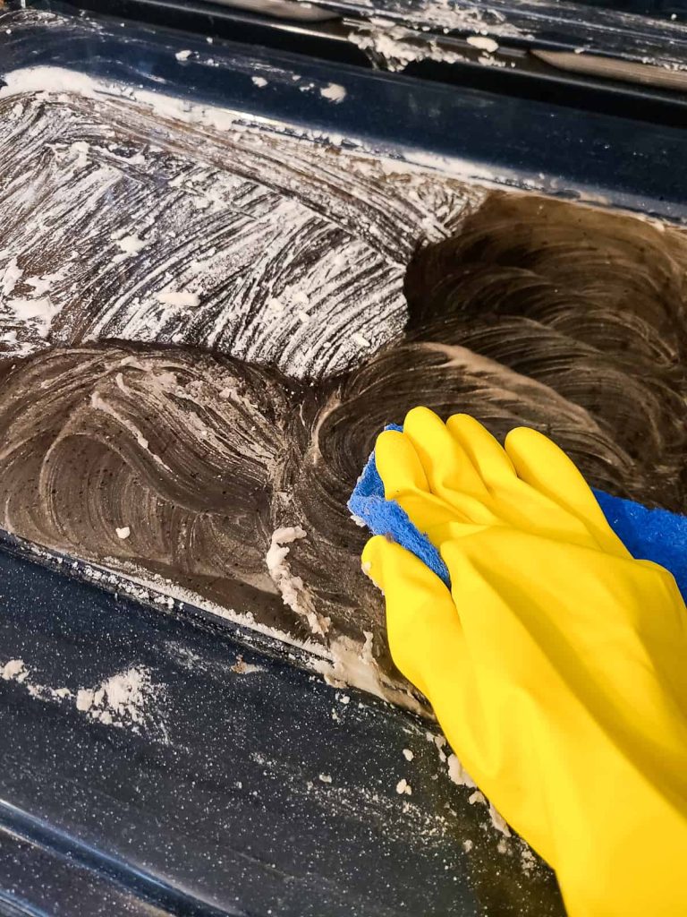 using gloves and a scour pad to scrub stains on the gas over door to clean off any debris left over from self cleaning
