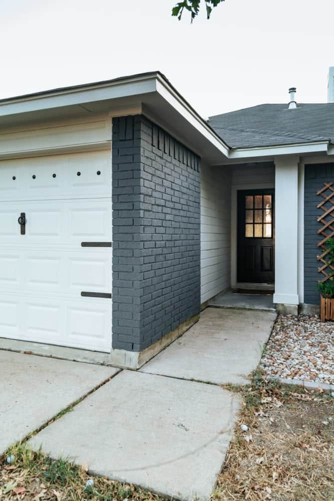 A black front door on a gray house with white contrast siding and garage door in an entryway