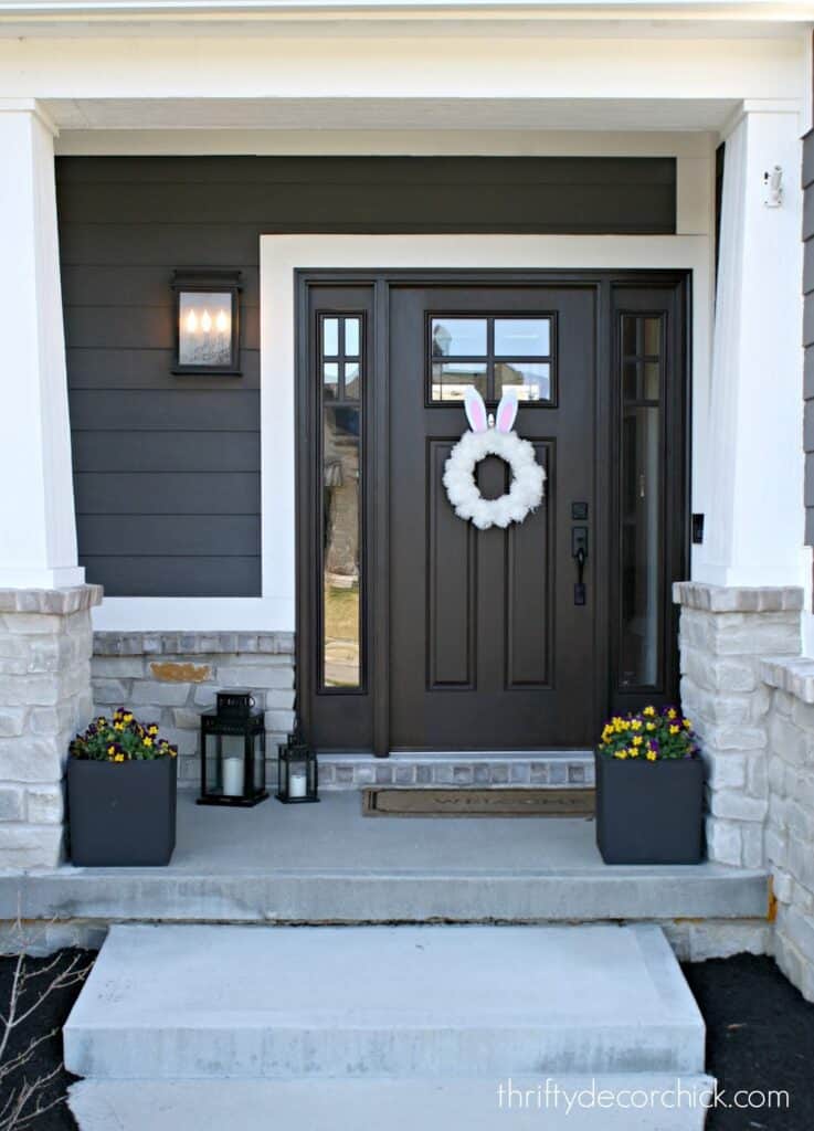 A wooden door on the front of a house used as the entry way done in a dark brown color on a gray house with white trim