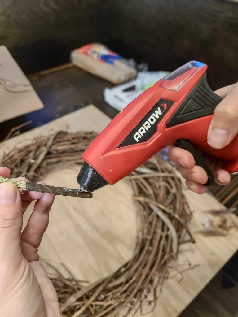 A photo of a person's hand attaching a pampas grass to wreath using a cordless hot glue gun