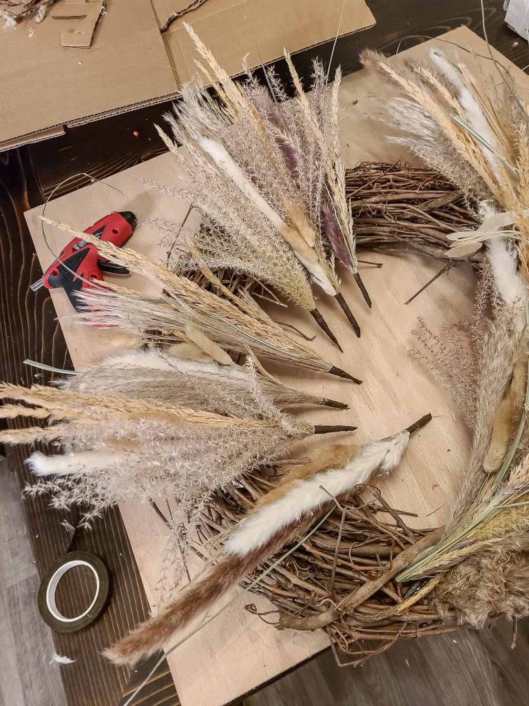 photo of Mixed Pampas grass wreath bundles laying on top of a grape vine wreath with hot glue gun in background