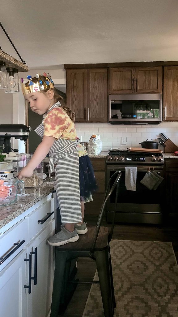 A young child was baking in the kitchen and used a chair as a step stool.