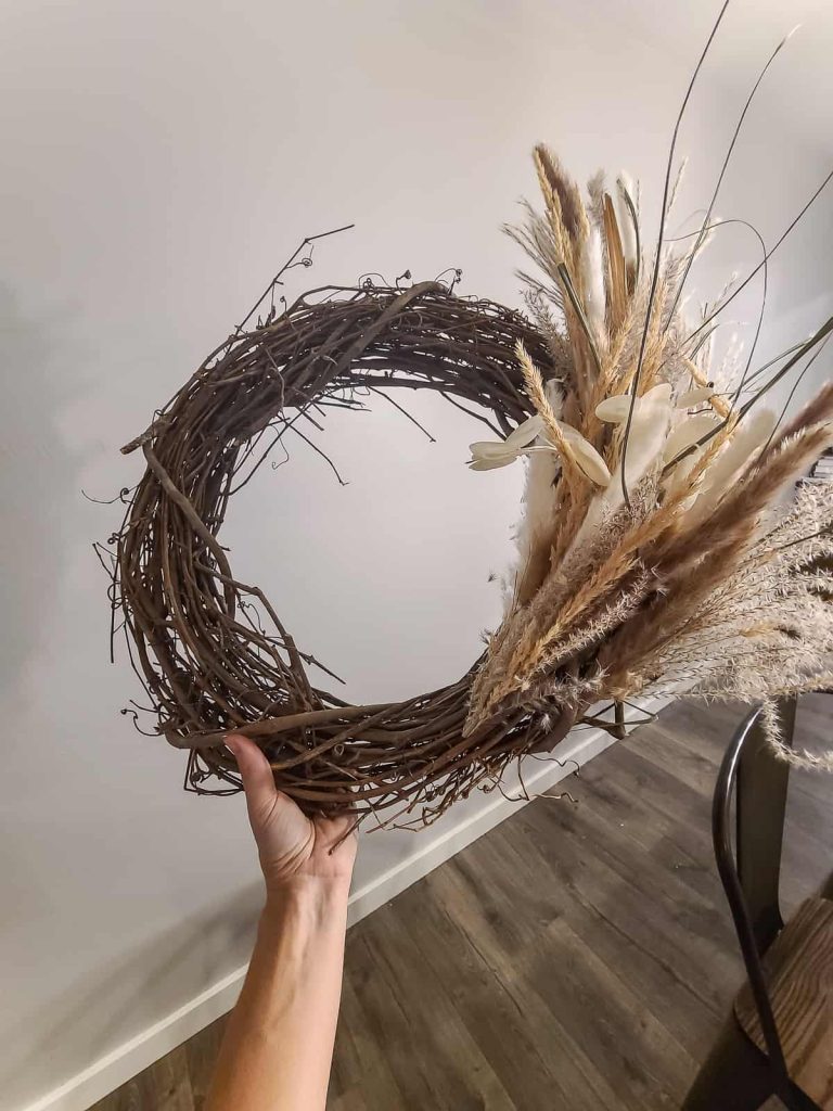 A person's hand holding unfinished pampas grass wreath