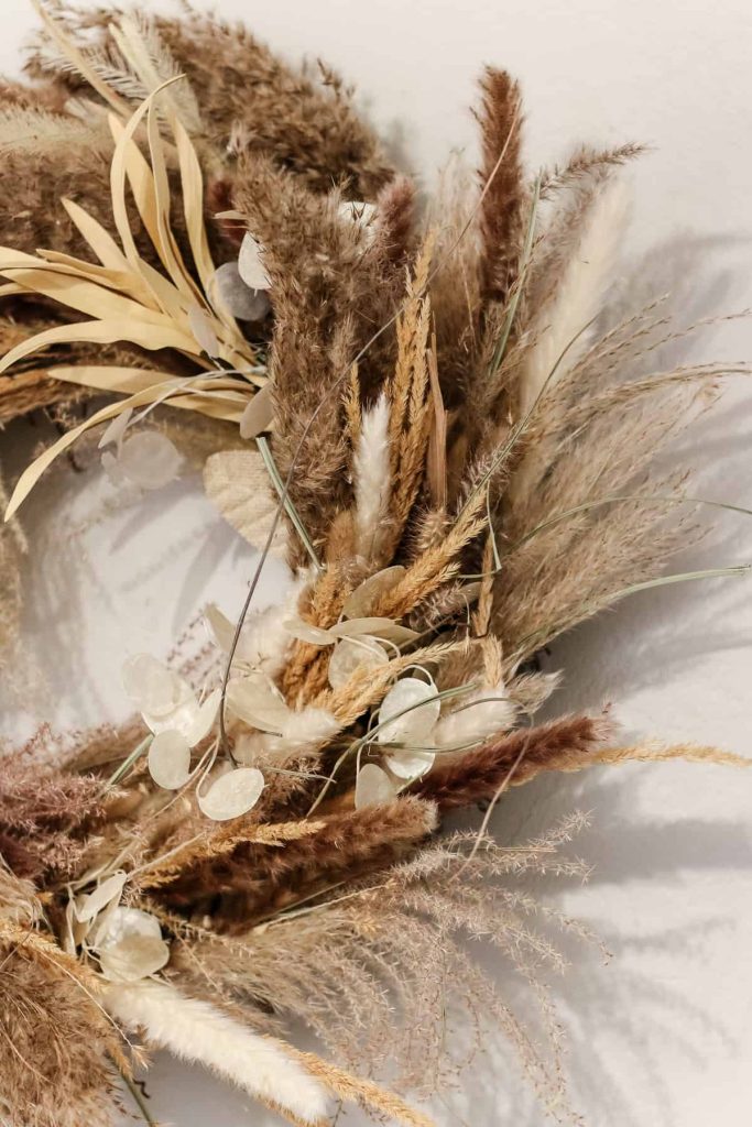 A photo of a wreath made from pampas grass hanging on the wall for easy fall decor