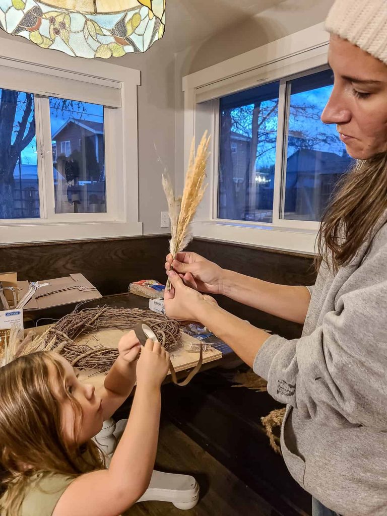 A picture of a women holding a pampas grass and her kid holding a floral tape while making a Mixed Pampas grass wreath.