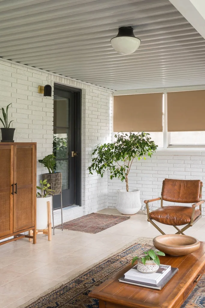 A beautiful photo of sunroom with white brick walls and mid-century modern furniture with a door painted with Behr Cracked Pepper 