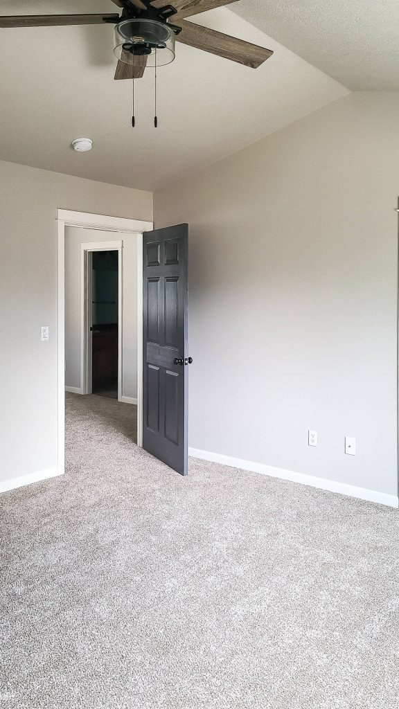 A photo of a black door with an elegant ceiling fan, light gray walls and off white trim