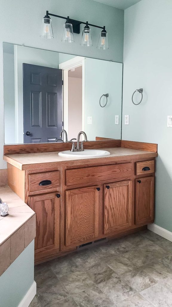A photo of a bathroom with a mirror, sink, and vanity light with light green paint color on the walls