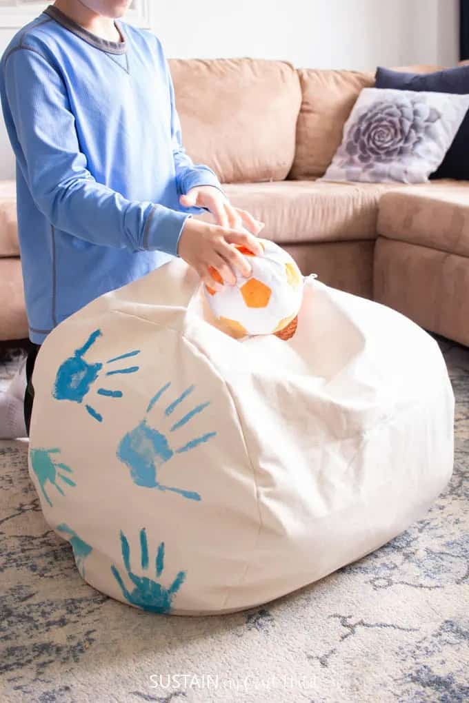 Boy putting stuffed animals into the DIY fabric storage ottoman