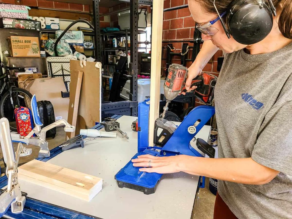 An individual operating a drill to fasten materials together for a DIY magazine shelf.