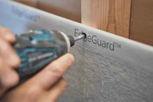 A person is nailing Durock board to the wall with a drill