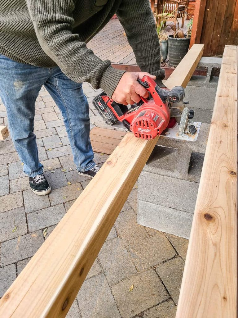 A man is using a circular saw to cut down a piece of 4x4 wood.