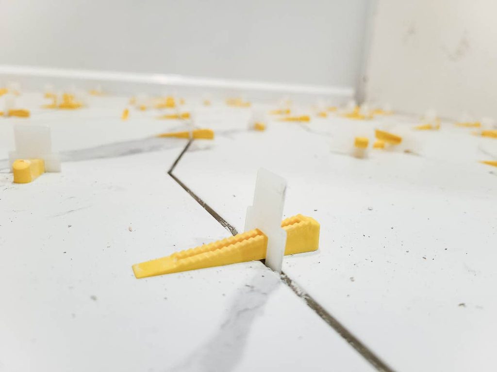An image showing applying grout between tiles identifying gaps using a grout float.