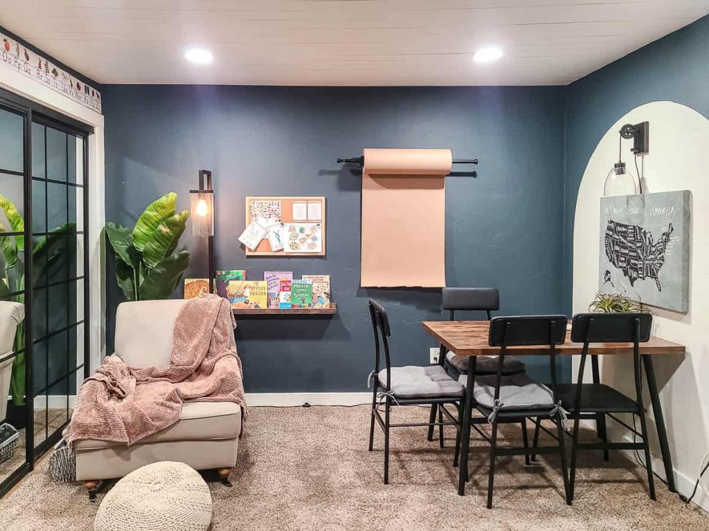 Comfortable learning space with built-in kraft paper holder, shelf displaying textbooks, and a cozy couch area with a table and chairs, providing a secure and inviting environment for educational activities.